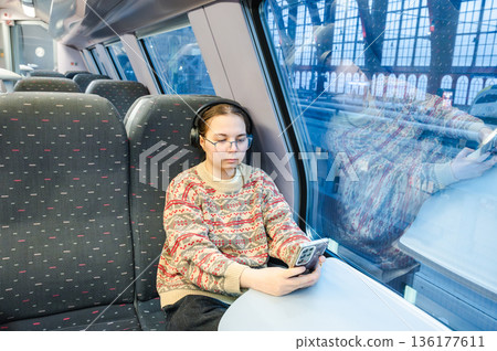 Smiling teenager girl with gallses and headphones in train Smiling teenager girl with gallses and headphones in train 136177611