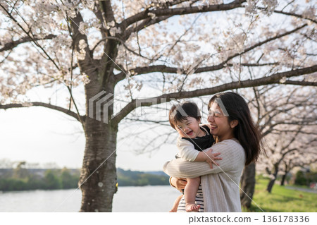 Mother and baby playing in a park with cherry blossoms 136178336