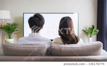 A man and a woman sit back to back on the sofa watching TV. Couples in a slump, communication, modern lifestyle 136178774