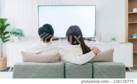 A man and a woman sit back to back on the sofa watching TV. Couples in a slump, communication, modern lifestyle 136178775