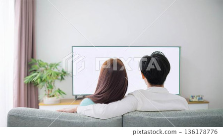 A man and a woman sit back to back on the sofa watching TV. Couples in a slump, communication, modern lifestyle 136178776