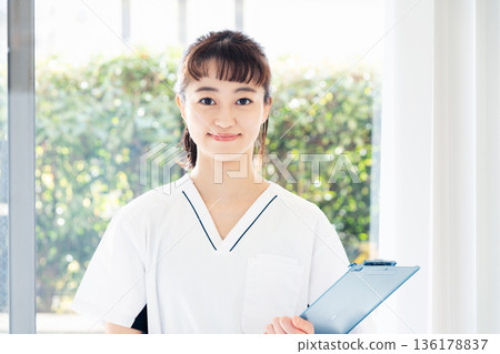 A female medical worker wearing a scrub and standing by the window A female medical worker wearing a scrub and standing by the window 136178837