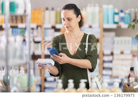 Woman in pharmacy scans QR code on gel for burns 136179975
