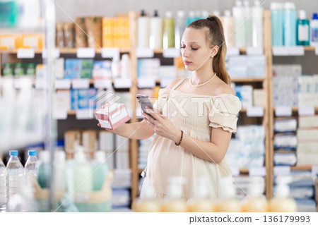 Pregnant woman customer scanning QR-code on pills box Pregnant woman customer scanning QR-code on pills box 136179993