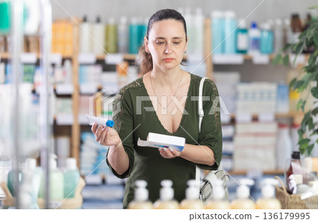 Woman in cardigan choosing ointment at pharmacy 136179995