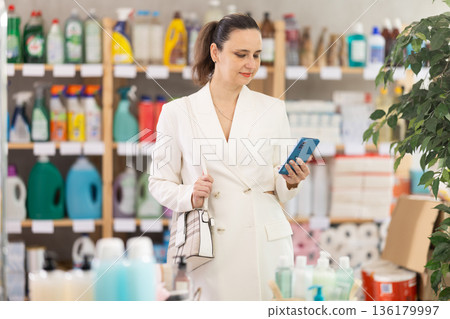 Adult woman with phone in household chemicals store Adult woman with phone in household chemicals store 136179997