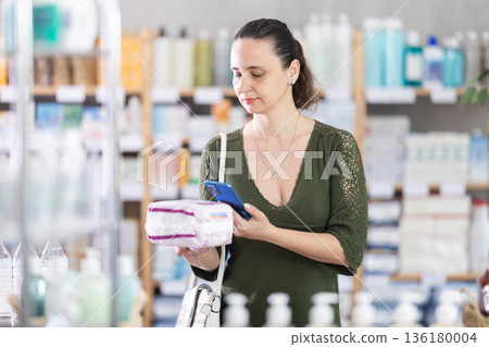Middle-aged woman scanning QR-code on feminine pads in drugstore Middle-aged woman scanning QR-code on feminine pads in drugstore 136180004