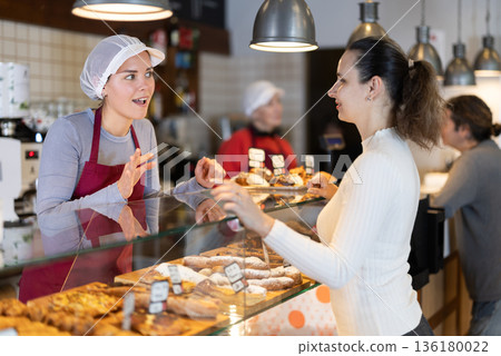 Bakery shop girl assistant talk to customer, answers questions and recommends fresh products Bakery shop girl assistant talk to customer, answers questions and recommends fresh products 136180022