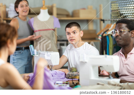 Young man stitching at machine during sewing class for adults Young man stitching at machine during sewing class for adults 136180032