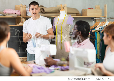 Young sewing instructor guiding adult beginners during practical workshop 136180069