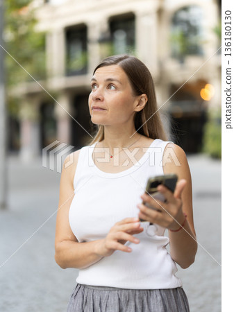 Female pedestrian with phone in summer European capital 136180130