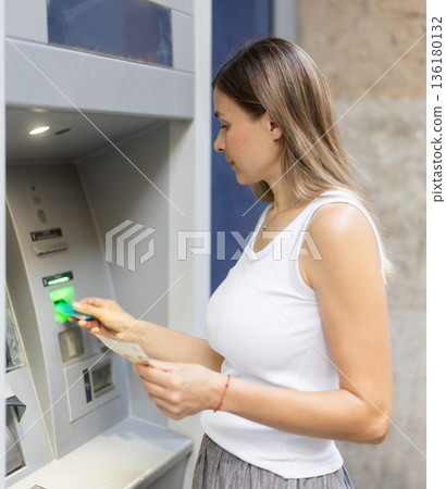 Woman uses outside ATM. Cash withdrawal, user interface Woman uses outside ATM. Cash withdrawal, user interface 136180132