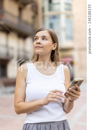 Female pedestrian with phone in summer European capital 136180155