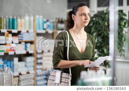 Middle-aged woman looking for medicaments according to prescription Middle-aged woman looking for medicaments according to prescription 136180163