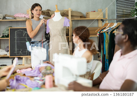Young sewing instructor guiding adult beginners during practical workshop Young sewing instructor guiding adult beginners during practical workshop 136180187