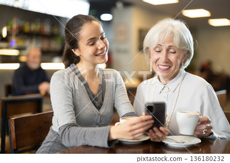 Elderly woman and her adult daughter having fun in cafe - looking at smartphone screen Elderly woman and her adult daughter having fun in cafe - looking at smartphone screen 136180232