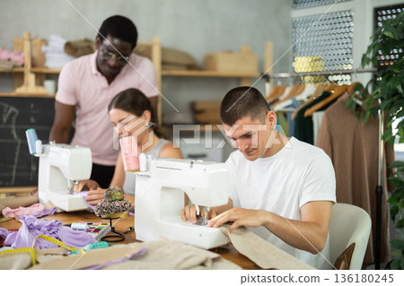 Engaged guy stitching fabric on machine in sewing class for adults 136180245