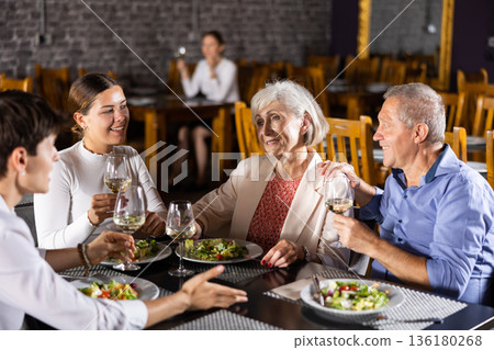 Young family and elderly couple of spouses eating in cafe celebrating event and communicating Young family and elderly couple of spouses eating in cafe celebrating event and communicating 136180268