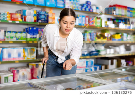 woman chooses nuggets in supermarket near showcase-refrigerator woman chooses nuggets in supermarket near showcase-refrigerator 136180276