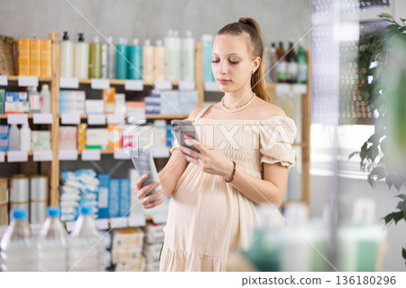 Young pregnant woman scanning QR-code on cream in drugstore 136180296