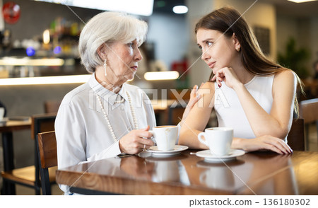 Elderly woman comforts an upset girl while sitting at table in cafe Elderly woman comforts an upset girl while sitting at table in cafe 136180302