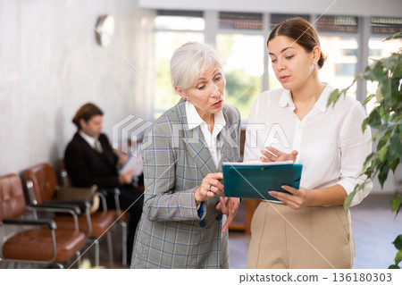 Young female office worker discussing papers with elderly woman 136180303