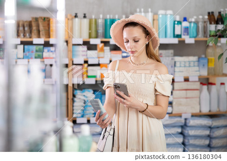Girl in summer clothes and hat scans code on sunscreen to check expiration date 136180304