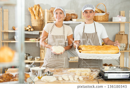Smiling young bakers standing in bakery with dough and baked baguettes 136180343