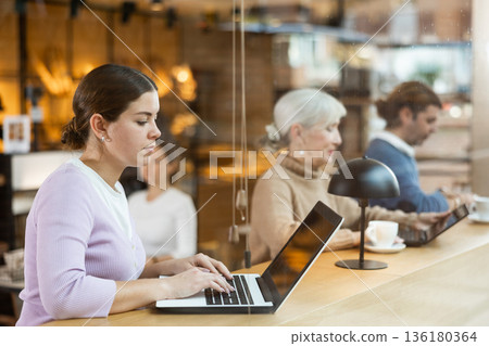 Smiling woman using laptop and drinking coffee in modern cafe 136180364