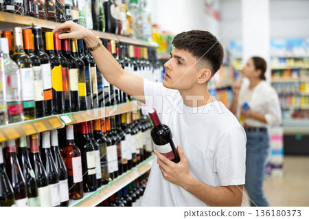 Thoughtful young guy choosing alcoholic drinks in supermarket Thoughtful young guy choosing alcoholic drinks in supermarket 136180373