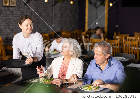 Waitress serving wine to senior couple having dinner in restaurant Waitress serving wine to senior couple having dinner in restaurant 136180385