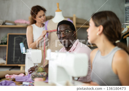 Middle-aged man talking with woman and sewing, other working with mannequin 136180473