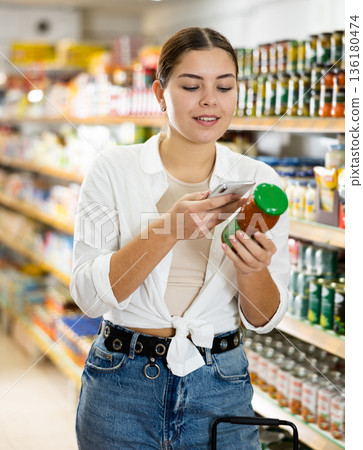 Young woman choosing preserved vegetables for herself in supermarket 136180474