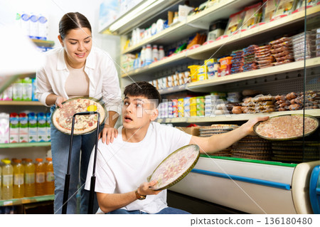 in supermarket in department of semi-finished products, couple chooses pizza 136180480