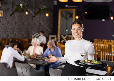 Young woman waiter posing with tray in restaurant Young woman waiter posing with tray in restaurant 136180493