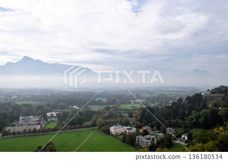Panoramic view of the foggy cityscape of the ancient city of Salzburg and the Alps from a high vantage point in Austria Panoramic view of the foggy cityscape of the ancient city of Salzburg and the Alps from a high vantage point in Austria 136180534