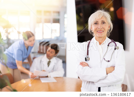 Confident smiling aged female doctor standing in medical office 136180617