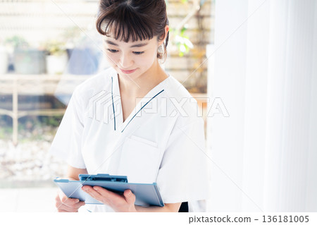 A female medical worker wearing a scrub and standing by the window 136181005