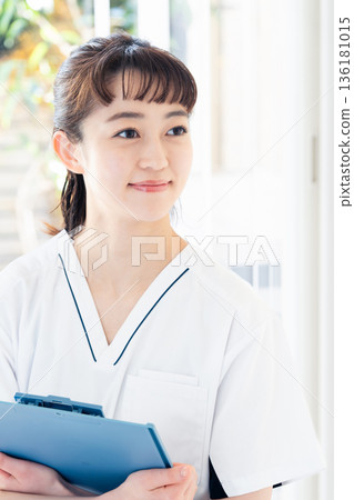 A female medical worker wearing a scrub and standing by the window A female medical worker wearing a scrub and standing by the window 136181015