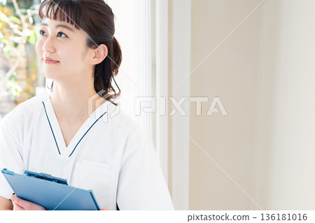A female medical worker wearing a scrub and standing by the window 136181016
