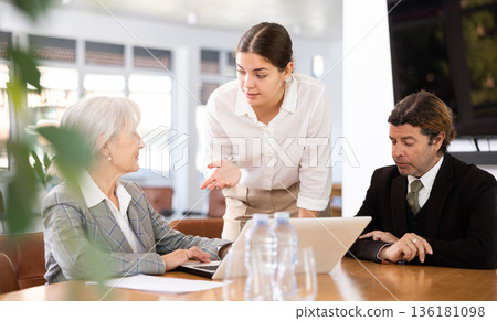 three positive office workers are sitting at table animatedly and actively discussing current work three positive office workers are sitting at table animatedly and actively discussing current work 136181098