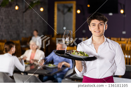 Smiling young waiter standing with serving tray in restaurant 136181105