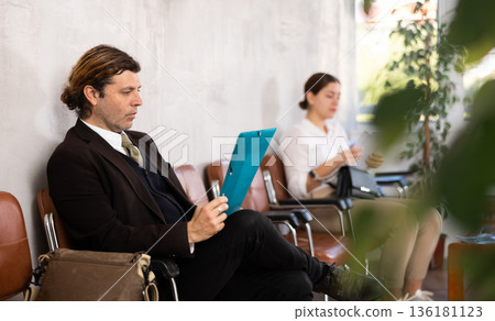 Confident entrepreneur with documents waiting for meeting with investors in office 136181123