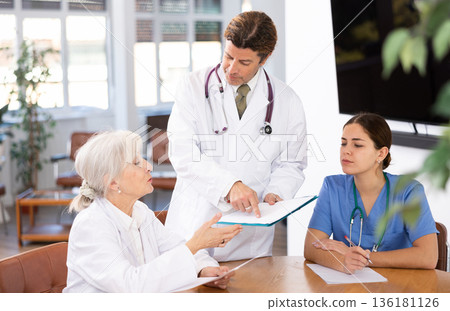 three positive doctors are sitting at table animatedly and actively discussing current work 136181126