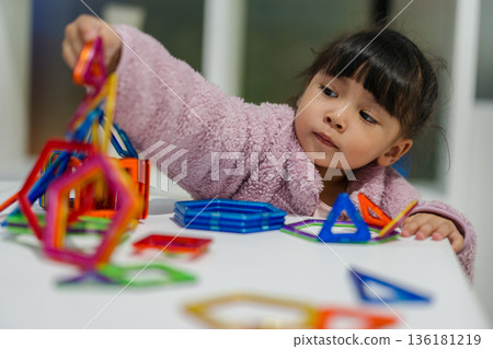 preschool child girl building structures with magnetic construction tiles. geometric shapes 136181219