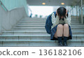 A worried Japanese female student sits on the stairs and holds her head 136182106