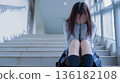 Unable to bear the loneliness, a Japanese high school girl covers her face and cries on the stairs 136182108