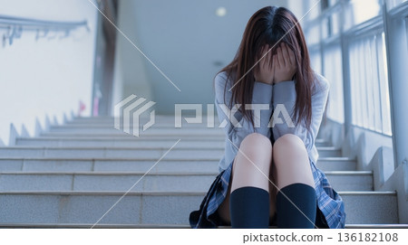 Unable to bear the loneliness, a Japanese high school girl covers her face and cries on the stairs 136182108