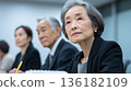 A senior female Japanese employee participating in a meeting with a serious look on her face 136182109