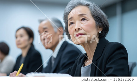 A senior female Japanese employee participating in a meeting with a serious look on her face 136182109
